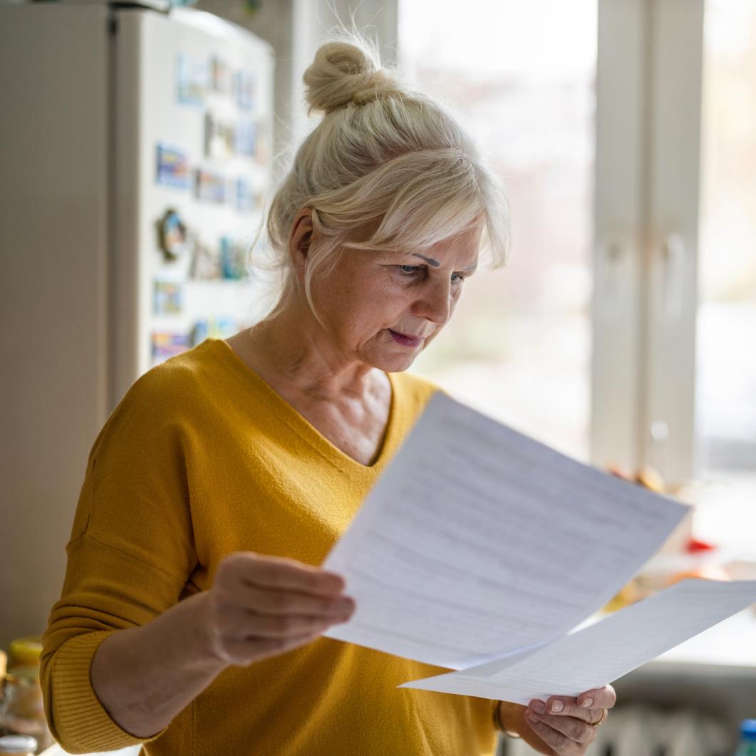 Ältere Dame im gelben Pulli mit Hochsteckfrisur liest in Dokumenten